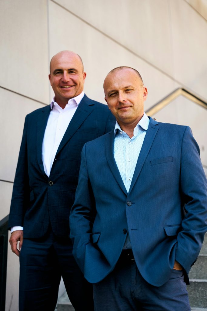 Two business professionals in modern suits posing confidently outdoors.